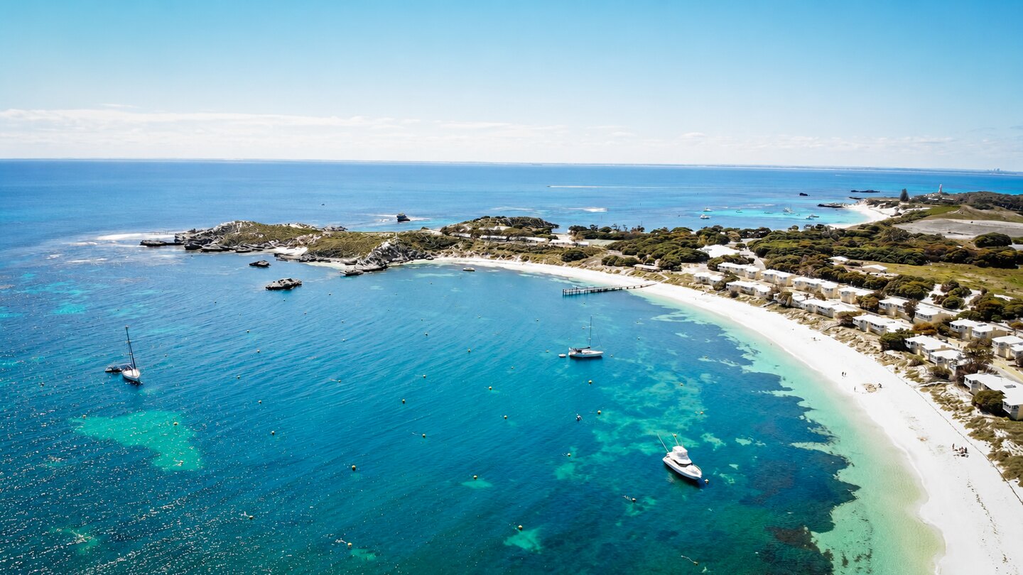 Horizontal aerial view across a white-sand bay, turquoise water and boats at Rottnest Island